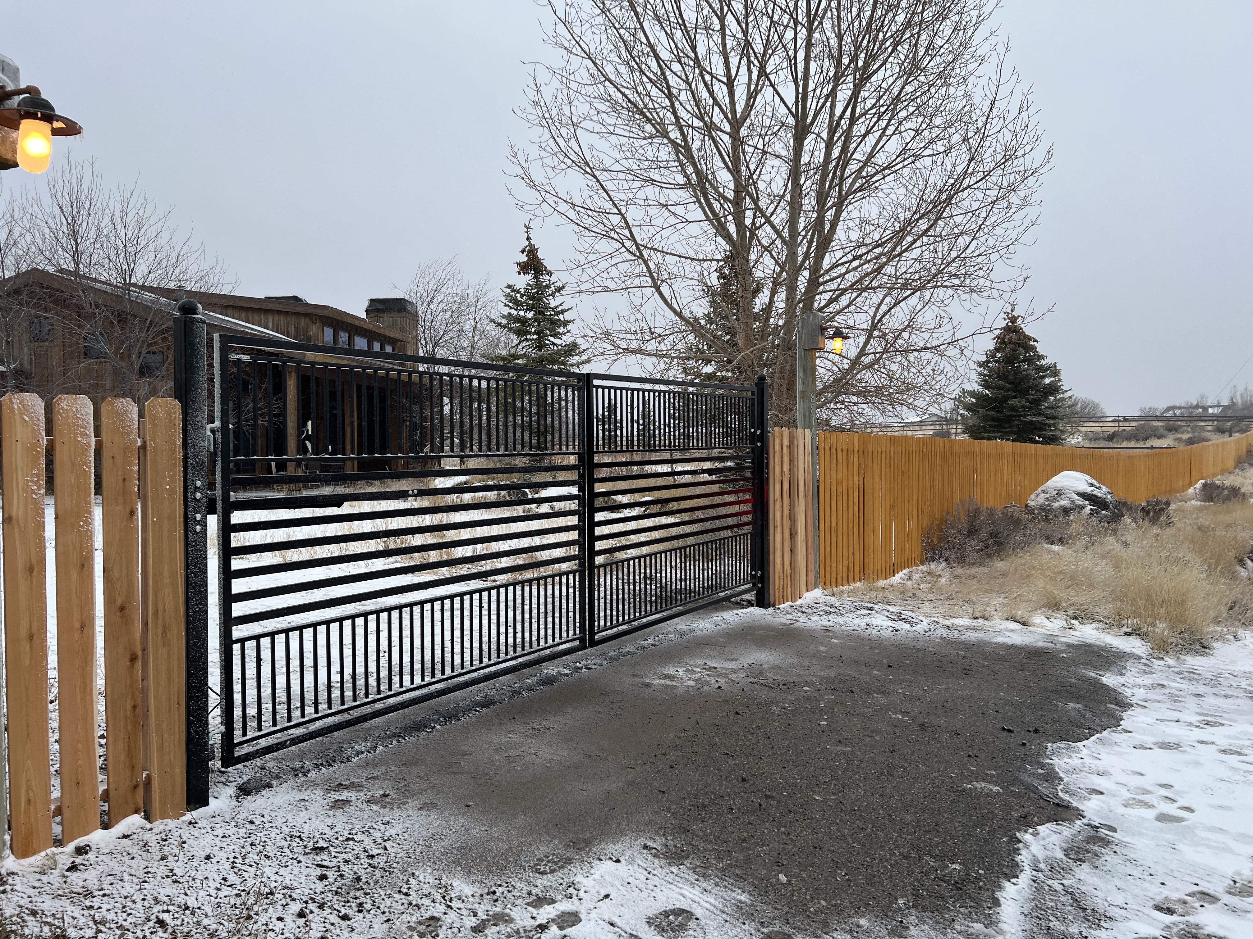 Automatic Gate installed in Park City Utah with black iron and matching posts with a an asphalt patch.